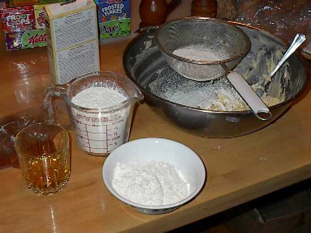 A bowl of dough, on the bowl is a sifter with sifted flour on top of the dough