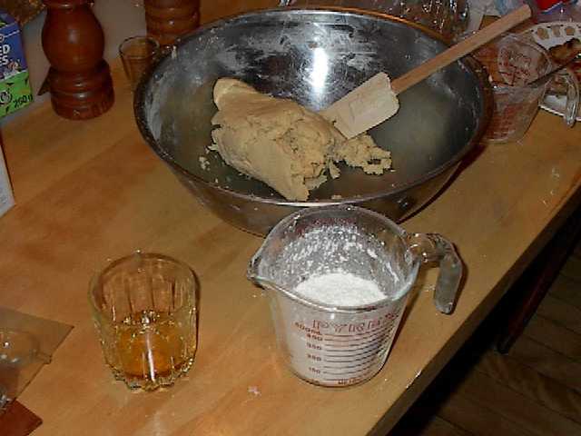 a ball of dough in a bowl with a measuring cup half full of flour and a glass of rye
